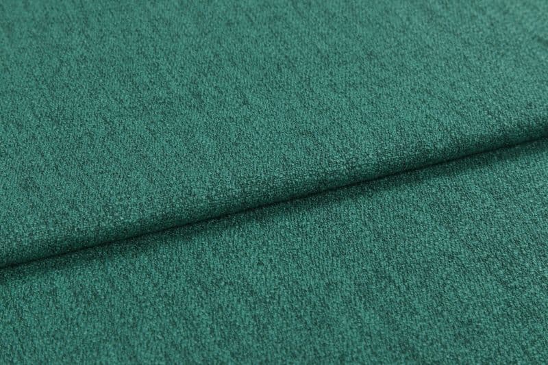 Teal-green textured upholstery fabric, close-up, showing short nap and subtle ribbing; folded horizontally with a visible overlap; photographed under soft, even lighting against an indistinct neutral background.