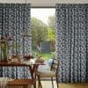 Full-length pleated geometric blue-gray curtains, drawn to sides and framing a central sliding glass door, filtering soft daylight; dining room with wooden table set for breakfast, pendant lamp, leafy backyard.