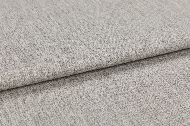 Woven light gray fabric folded in overlapping layers, showing subtle texture and flecked yarns; photographed close-up with soft, even studio lighting on a neutral surface.