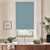 Blue roller blind covers most of a kitchen window, blocking light; stainless faucet and sink sit below on a countertop with a bowl of vegetables, potted plants and framed sketch.