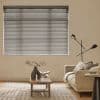 Horizontal venetian blinds covering a large wall window, slats mostly closed and filtering soft daylight; beige living room with sofa, wooden coffee table, patterned rug and black floor lamp.