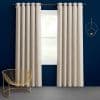 Beige grommet-top curtains hung on a metal rod, drawn to frame a central window and softly filtering daylight; navy-painted wall, gold wire chair, circular wall sconce in a minimal room.