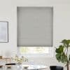 Grey textured roller blind fully lowered, blocking most light; minimalist dining nook with round table, glassware and vase, potted fiddle‑leaf fig, soft daylight filtering around blind edges.