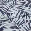 Navy textile printed with pale-blue palm-leaf motif, folded across the center producing an overlapping seam; close-up studio view highlighting fabric texture and even, soft lighting.