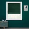 Dark green Roman blind, centered in white window frame, folded slightly near the bottom and covering most glass; teal-painted room with a small dresser left and framed abstract art right.