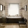White pleated roller blind fully lowered over window, diffusing soft daylight; below, an alcove bathtub set in dark wood surround, beige horizontal-striped walls, floating shelf with toiletries, woven chair.