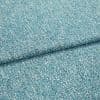 Textured teal woven fabric, folded once across the frame, showing speckled weave and edge detail; close-up studio-lit shot emphasizing material texture.