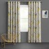 Grommet-top, full-length floral curtains (yellow, blue, gray leaves) hang pulled slightly aside on a metal rod, filtering daylight and framing the window in a gray-walled room with gold wire chair.