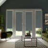 White French doors with gray roller blinds lowered halfway, filtering daylight into a modern living room framed by green velvet armchairs, glass coffee table atop zigzag rug, garden visible outside.