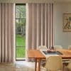 Blush-and-cream checkered full-length curtains, mostly drawn with a narrow central gap; allowing light to frame a mullioned window and green garden, in a sunlit dining room with wooden table.