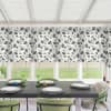 Floral-panel blinds cover upper windows; they hang above a dining table set with plates, green glassware and candles, surrounded by green upholstered chairs, with a grassy backyard visible below.