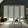 French doors with lowered light-gray roller blinds, letting a narrow garden view at the bottom; set in a dark-painted living room with green armchairs, glass coffee table on a chevron rug.