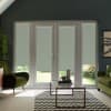 Glass double doors are covered by pale roller blinds, framing a garden view; in front, a glass coffee table on a black-and-white chevron rug, flanked by green velvet armchairs.