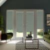 Patterned roller blinds cover French doors and sidelights, filtering daylight into a modern living room with green armchairs, glass coffee table on a black-and-white chevron rug, garden visible beyond.