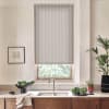Roller blind hangs partly lowered over a kitchen window, filtering light; metal faucet and sink sit below on wooden countertop with potted plants, bowl of greens, and artwork.