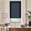 Navy roller blind covering upper portion of a kitchen window, partially lowered; stainless faucet and double sink below on a marble countertop with wooden cabinets, bowl of greens, potted plants.