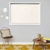 Vertical cream blinds covering a window, fully closed with decorative bead chain along the bottom, filtering soft daylight; mounted on a grey living-room wall above mustard rug, chair and table.