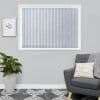Vertical fabric blinds covering a window, closed and softly diffusing light; gray living room with framed botanical print, potted plant, gray armchair with pillow and knit throw, patterned rug.