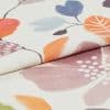 Folded floral-printed textile, two layered panels with pastel orange, blue and purple leaf motifs; folded edge overlaps the lower layer. Close-up, studio-lit view highlighting woven texture and soft, neutral lighting.