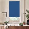 Blue roller blind covers a window above a kitchen sink. Stainless faucet sits in a countertop with wooden cabinets below, bowls of greens, potted plants and a framed sketch nearby.