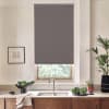 Gray roller blind hangs lowered over a window, revealing treetops below; stainless faucet and double sink sit on a marble countertop with bowls of leafy greens and potted plants.