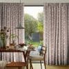 Full-length pleated curtains with a pink squiggle pattern, parted to reveal sliding glass door and gently filtering daylight; framing a wood dining table set for breakfast and sunlit garden beyond.