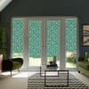 Glass patio doors fitted with green floral roller blinds, framing a sunlit garden; set within a modern living room with olive armchairs, glass coffee table, zigzag rug, and potted plants.