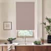 A pink patterned roller blind covers a window above a kitchen sink, surrounded by pale walls, wooden cabinets, a chrome faucet, potted plants, a bowl of greens, and a small framed sketch.