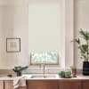 Window roller blind covers upper half of a kitchen window above a stainless sink; faucet centered on stone countertop with bowls of leafy greens, potted plants and framed sketch.