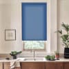 Blue roller blind covers most of a kitchen window, filtering daylight; below, a stainless faucet and sink sit on a marble countertop with bowls of leafy greens and potted plants.