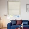 Beige honeycomb pleated blind, lowered over window with subtle horizontal texture; partially raised, filtering soft daylight into a modern living room with blue sofa, floor lamp and framed abstract art.