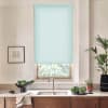 Light blue roller blind covers the upper portion of a kitchen window, filtering light above a sink and faucet; countertop holds bowls of greens, a towel, potted plants, and a framed sketch.