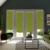 French glass doors with green roller blinds partially lowered, framing a sunlit garden outside; modern living room around them with green armchairs, glass coffee table, chevron rug, and potted plants.
