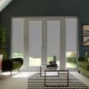 Patio glass doors covered by lowered grey roller blinds, revealing narrow garden view below; set in a living room with green armchairs, glass coffee table on a black-and-white chevron rug.