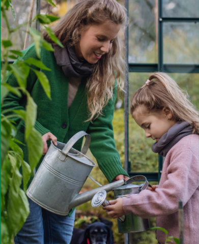 Mother and child watering plants in a greenhouse